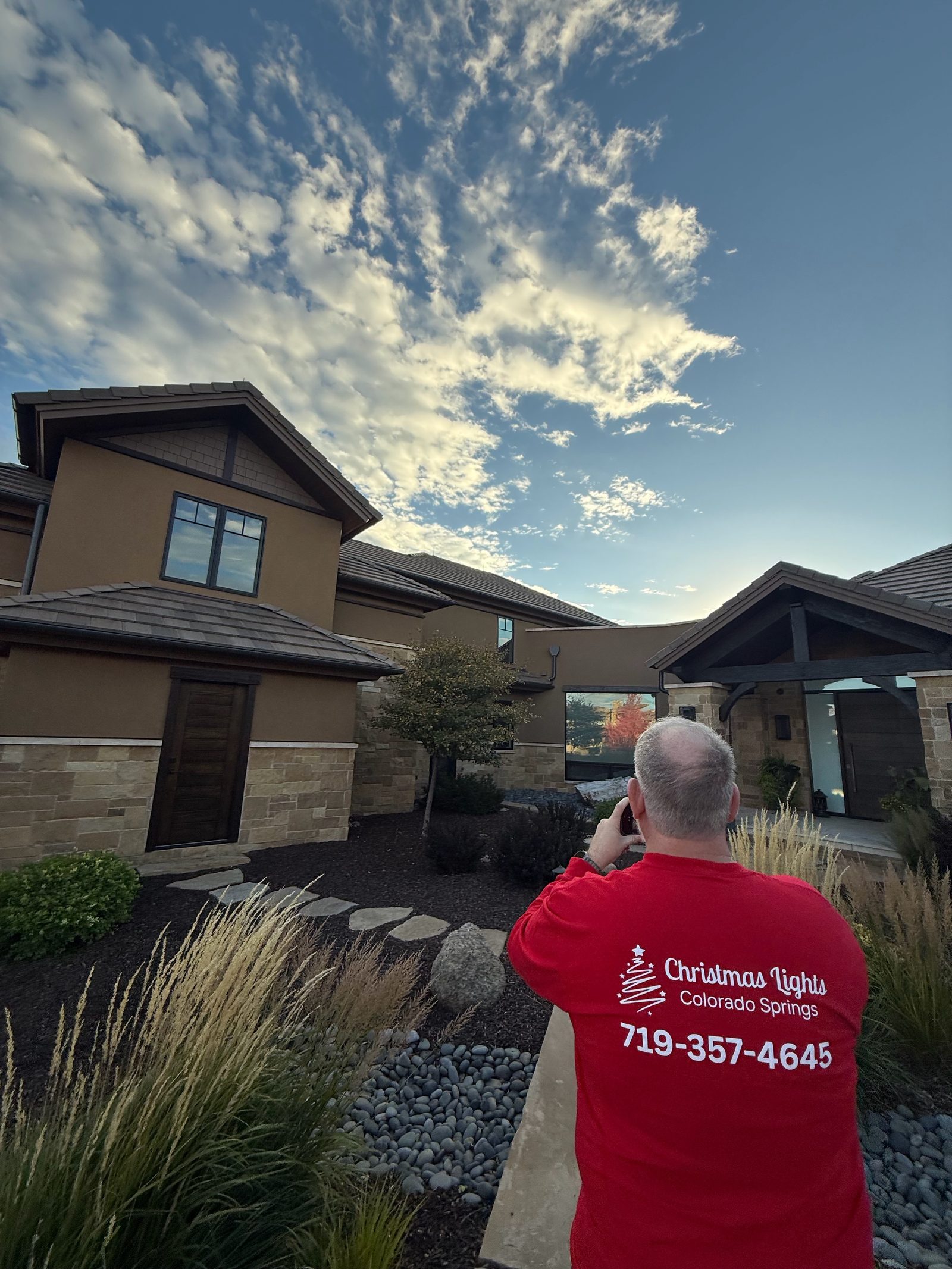 Christmas Lights Colorado Springs technician in branded shirt photographing a finished holiday lighting install