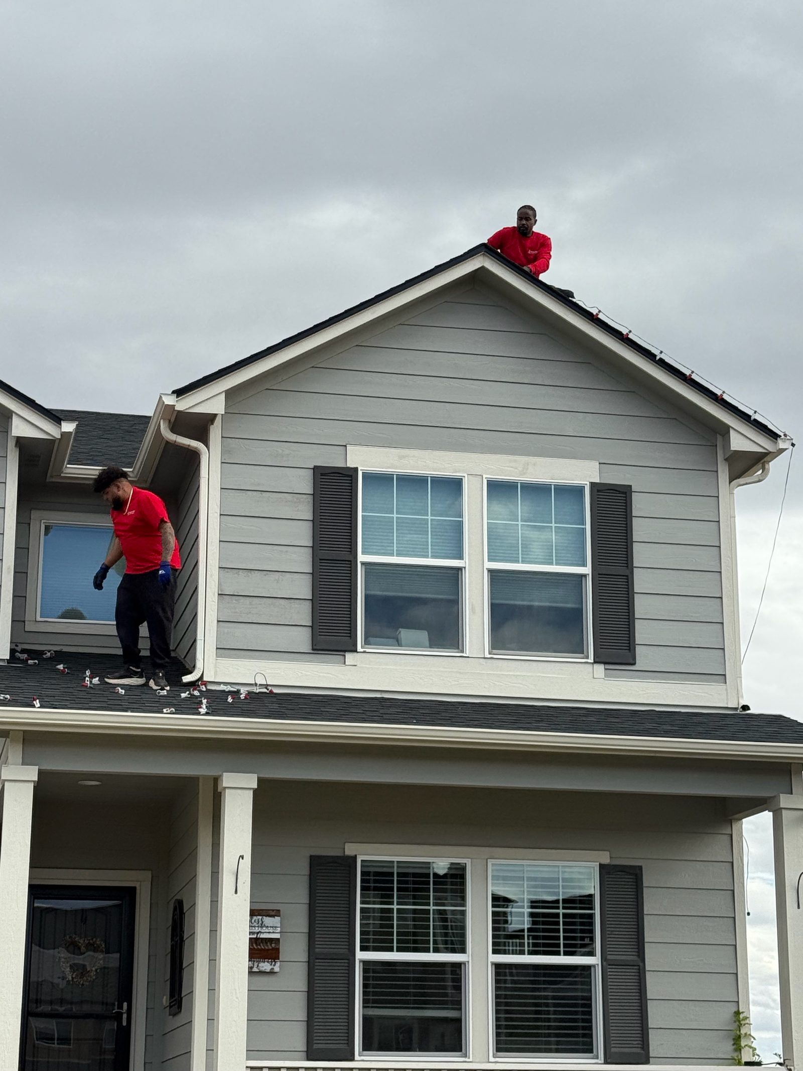 Christmas Lights Colorado Springs installers on roof peak hanging holiday lights on a gray Front Range house