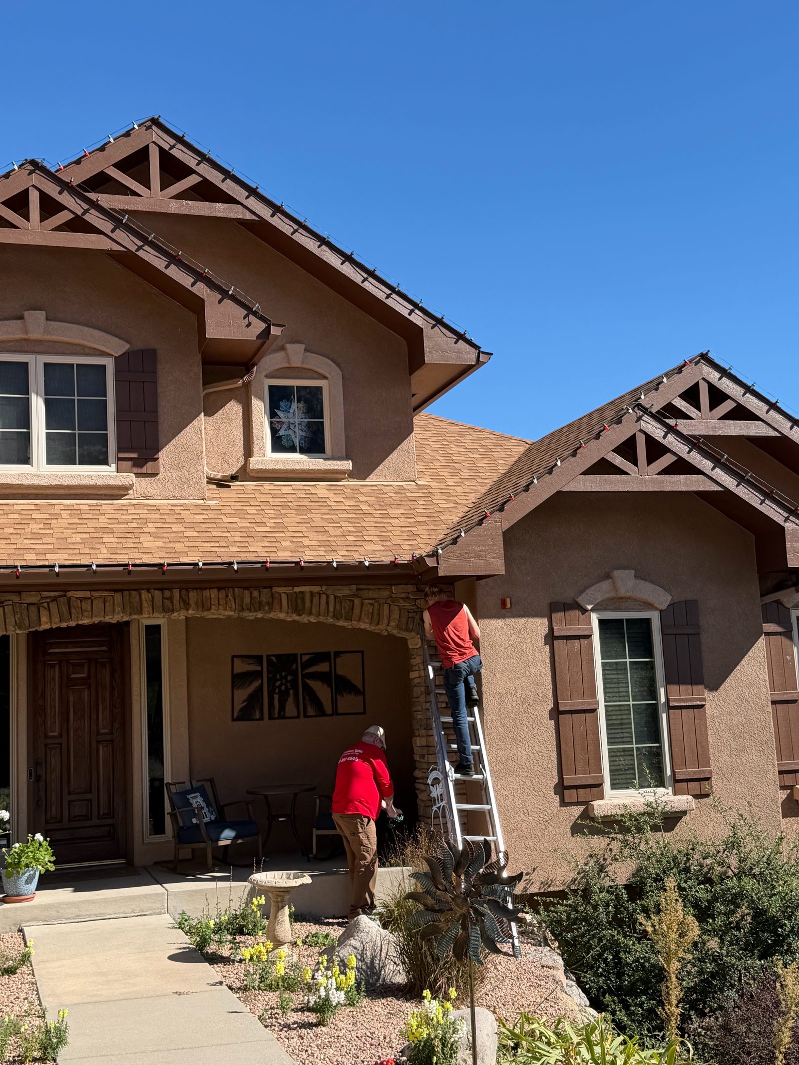 Christmas Lights Colorado Springs crew on ladder installing roofline Christmas lights by the front porch