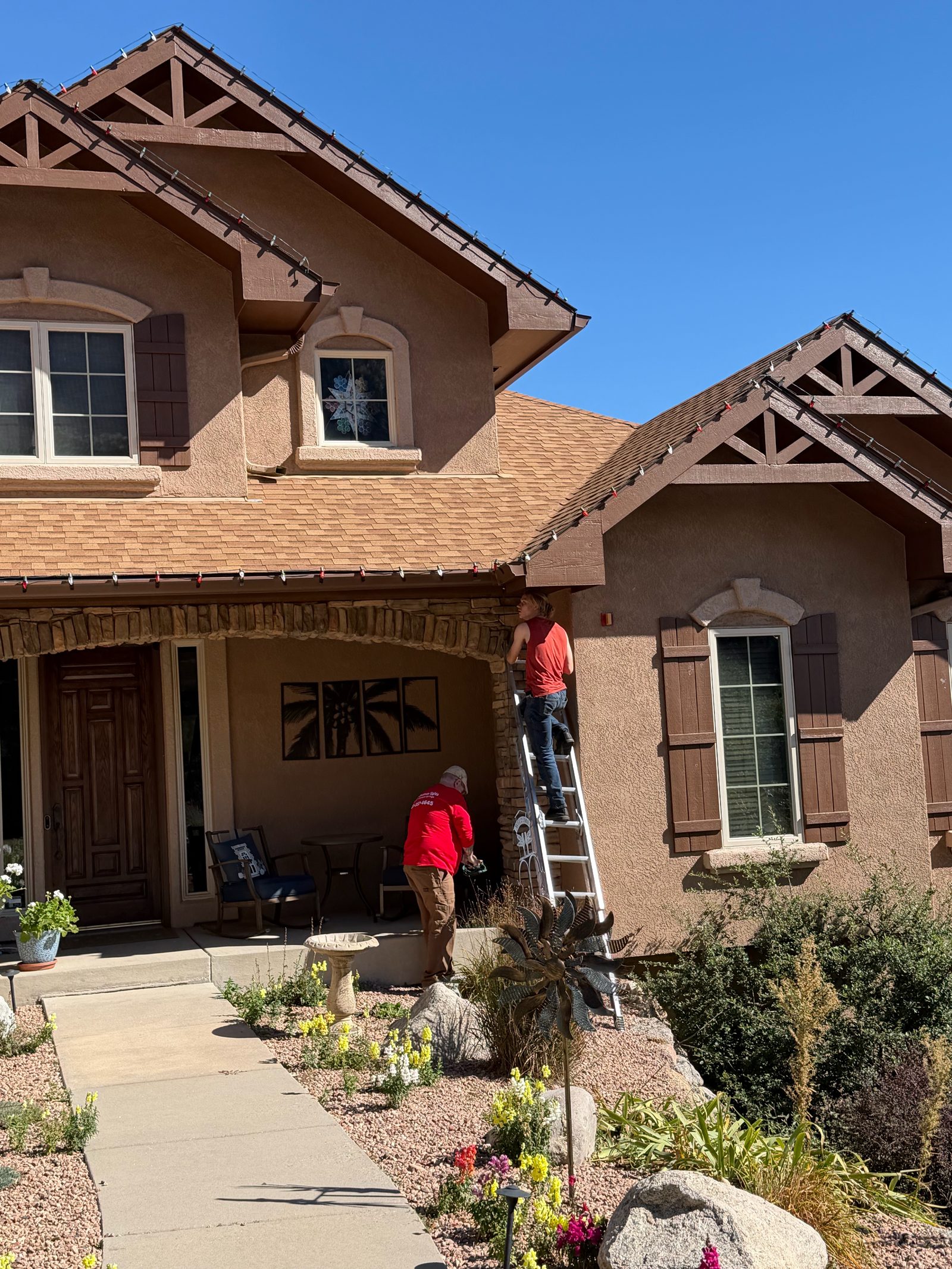Christmas light installers on ladder hanging red Christmas lights on a Colorado Front Range home